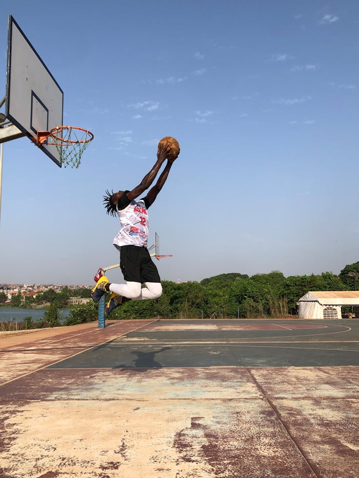 Athlete performing a powerful dunk on an outdoor basketball court under a clear blue sky.