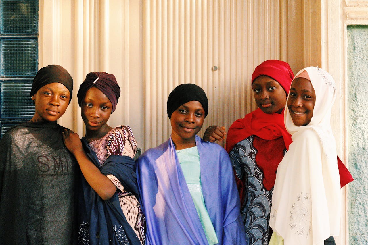 Five young girls in colorful hijabs smiling together outdoors in Abuja, Nigeria.