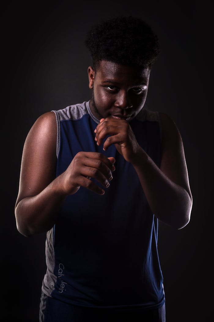 A young African American boxer poses confidently in a dark studio setting, ready for action.